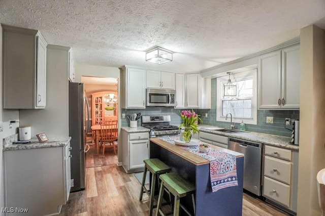 kitchen with light wood finished floors, a sink, stainless steel appliances, light countertops, and backsplash