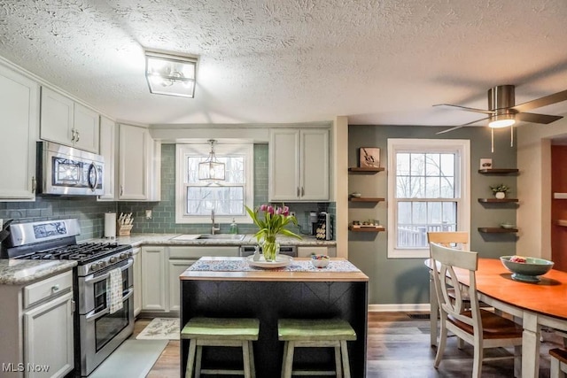 kitchen with wood finished floors, a sink, light stone countertops, stainless steel appliances, and backsplash