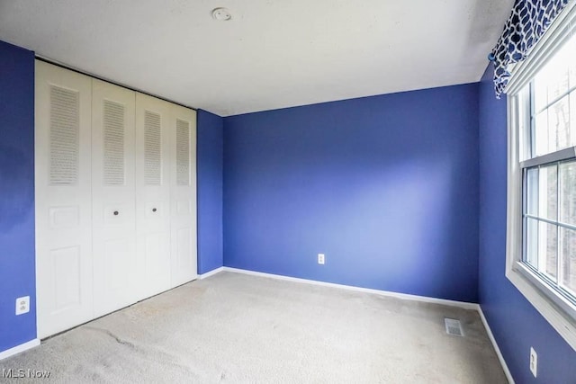 unfurnished bedroom with carpet floors, multiple windows, visible vents, and baseboards