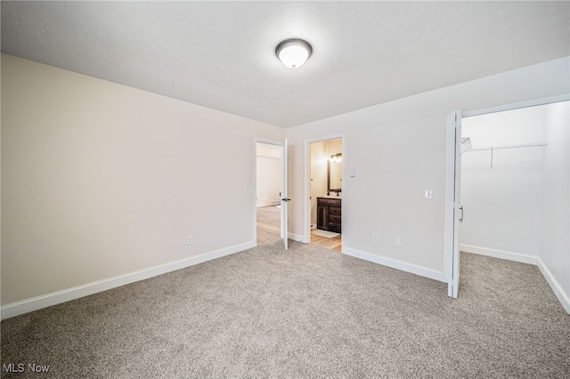 unfurnished bedroom featuring light carpet, baseboards, a spacious closet, a textured ceiling, and a closet