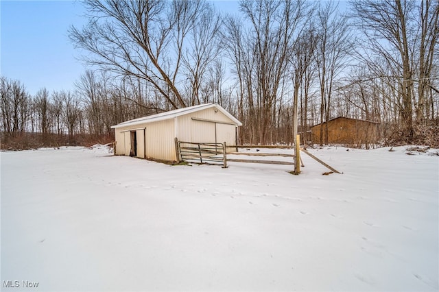 snow covered structure with fence and an outbuilding