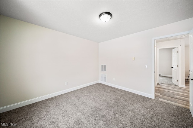 unfurnished room featuring carpet, a textured ceiling, baseboards, and attic access