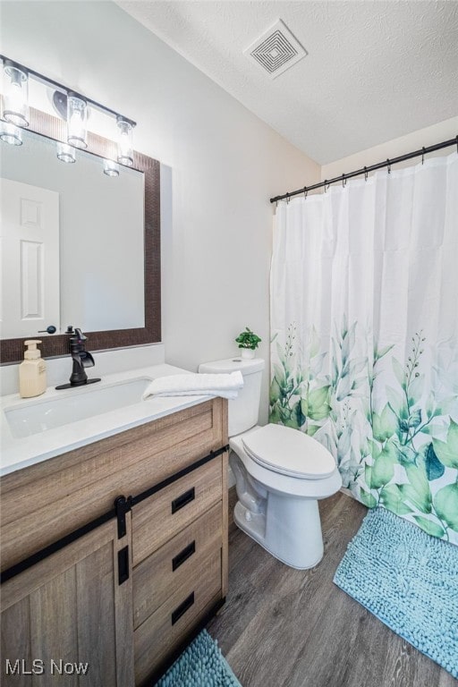 bathroom featuring a textured ceiling, toilet, wood finished floors, vanity, and visible vents