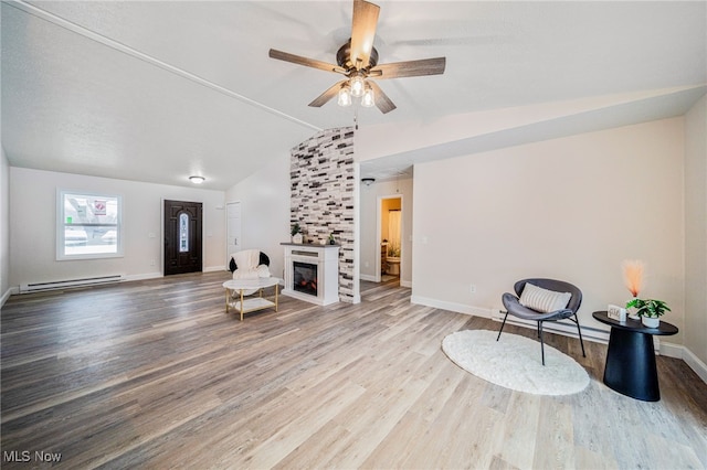 sitting room with a baseboard heating unit, vaulted ceiling, wood finished floors, a lit fireplace, and baseboards