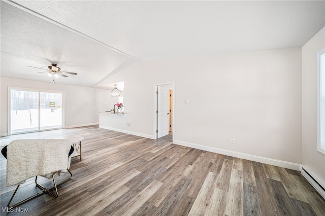 unfurnished living room featuring vaulted ceiling, baseboard heating, wood finished floors, and baseboards