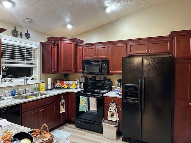 kitchen featuring lofted ceiling, a sink, dark brown cabinets, light stone countertops, and black appliances