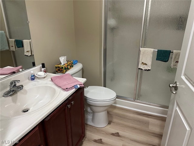 bathroom with toilet, a stall shower, wood finished floors, and vanity