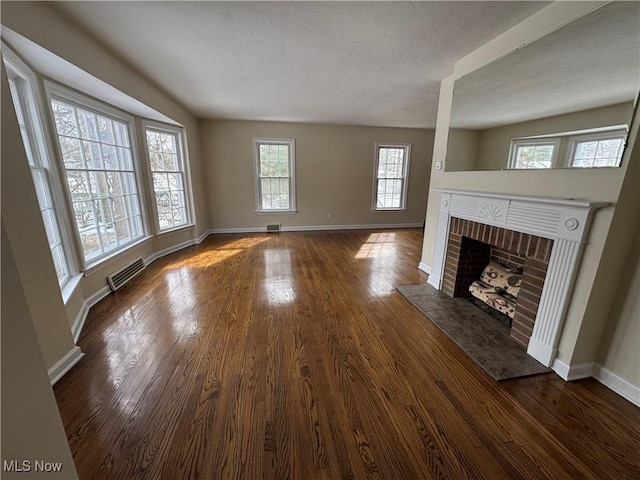 unfurnished living room with a fireplace, dark wood finished floors, visible vents, and baseboards