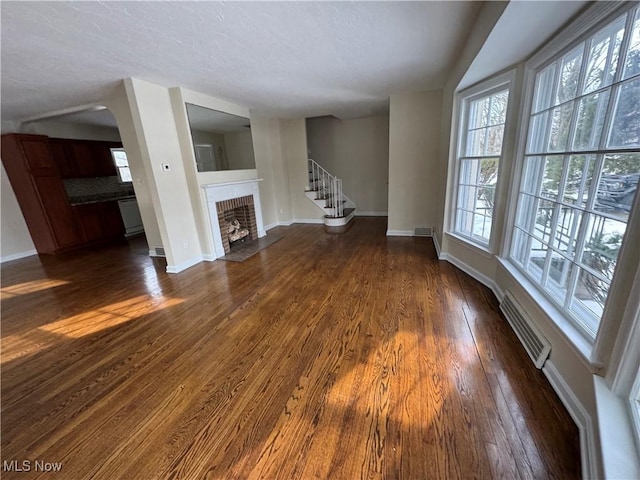 unfurnished living room with dark wood-style flooring, a fireplace, visible vents, baseboards, and stairs