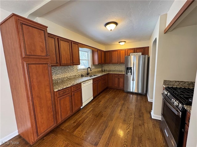 kitchen featuring dark wood-type flooring, a sink, light stone countertops, stainless steel appliances, and backsplash