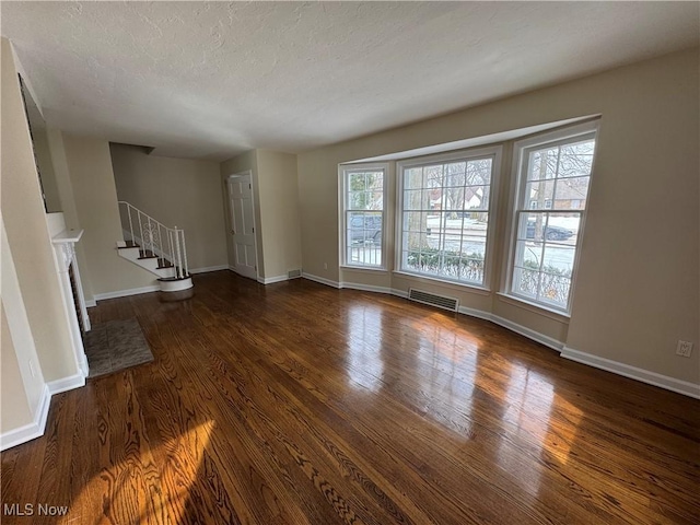 unfurnished living room featuring a fireplace, visible vents, stairway, a textured ceiling, and wood finished floors