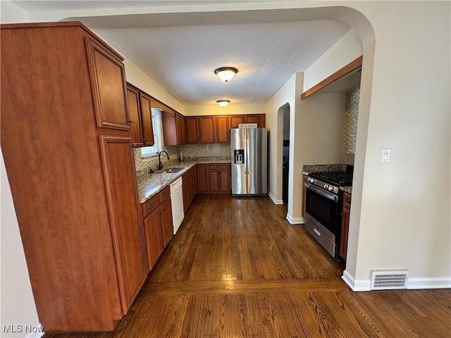 kitchen with light stone counters, arched walkways, stainless steel appliances, visible vents, and a sink