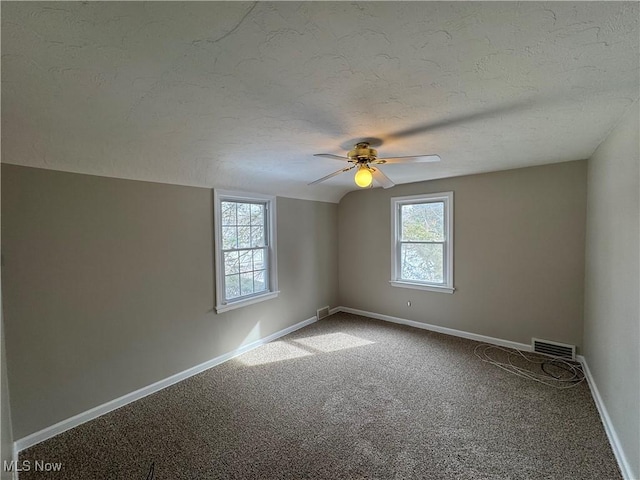 unfurnished room with a textured ceiling, a wealth of natural light, carpet, and visible vents