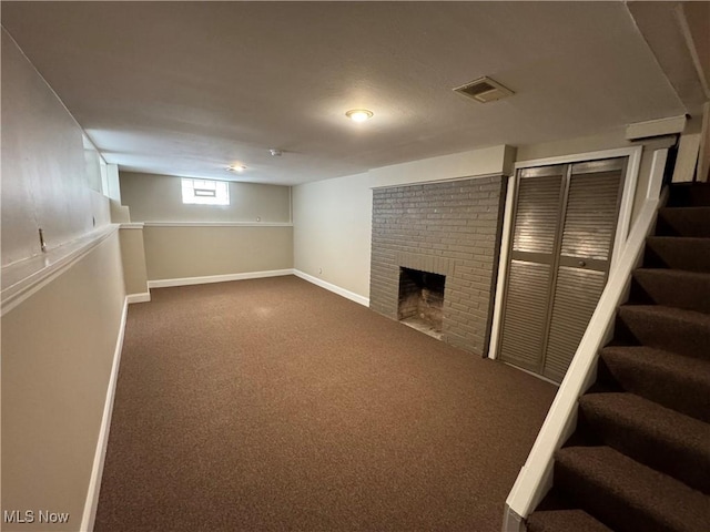 below grade area featuring visible vents, baseboards, stairway, dark colored carpet, and a fireplace