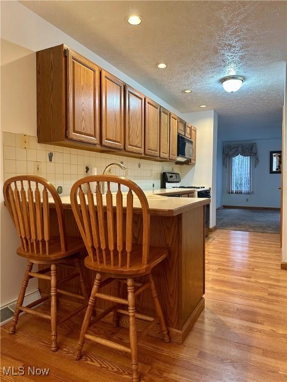 kitchen with brown cabinetry, black microwave, a peninsula, and light wood finished floors