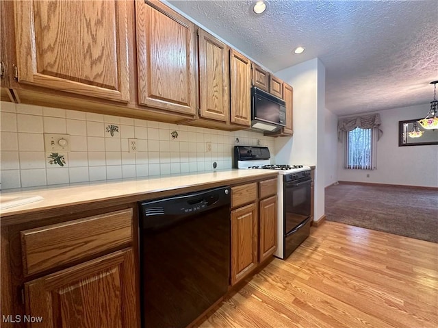 kitchen with light countertops, a textured ceiling, light wood-type flooring, black appliances, and backsplash