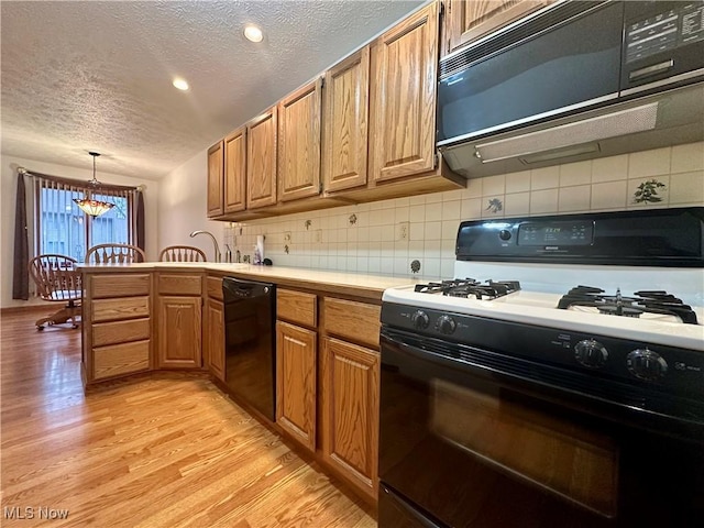 kitchen with a peninsula, light countertops, light wood-type flooring, decorative backsplash, and black appliances