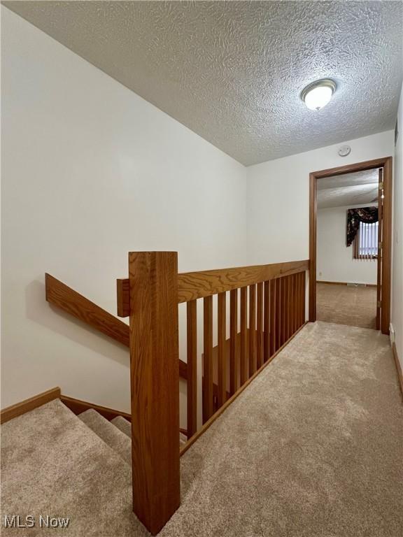 corridor with carpet, baseboards, a textured ceiling, and an upstairs landing