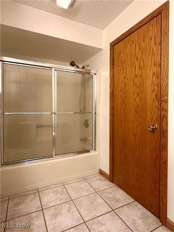 bathroom featuring bath / shower combo with glass door, a textured ceiling, and tile patterned floors