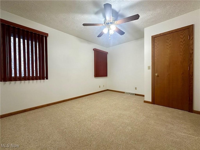 carpeted empty room featuring a ceiling fan, baseboards, visible vents, and a textured ceiling