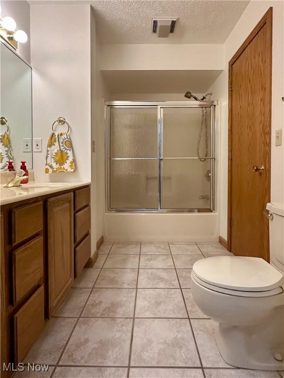 full bath with visible vents, toilet, shower / bath combination with glass door, a textured ceiling, and vanity