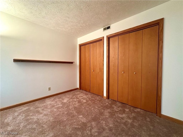 unfurnished bedroom featuring carpet floors, baseboards, visible vents, and two closets