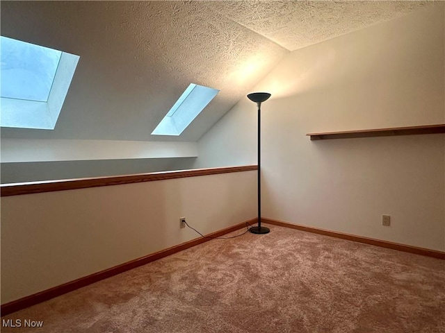 additional living space featuring carpet floors, lofted ceiling with skylight, baseboards, and a textured ceiling