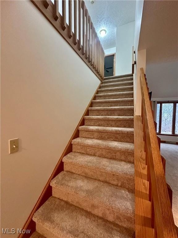 staircase with carpet floors, baseboards, and a textured ceiling