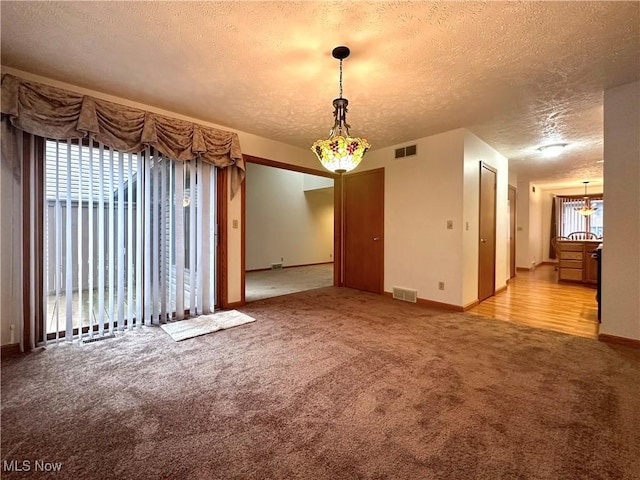 carpeted empty room with baseboards, visible vents, and a textured ceiling