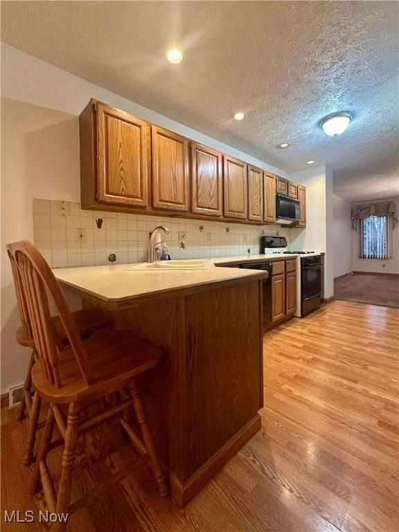 kitchen with range with gas cooktop, decorative backsplash, brown cabinetry, light wood-style floors, and a peninsula