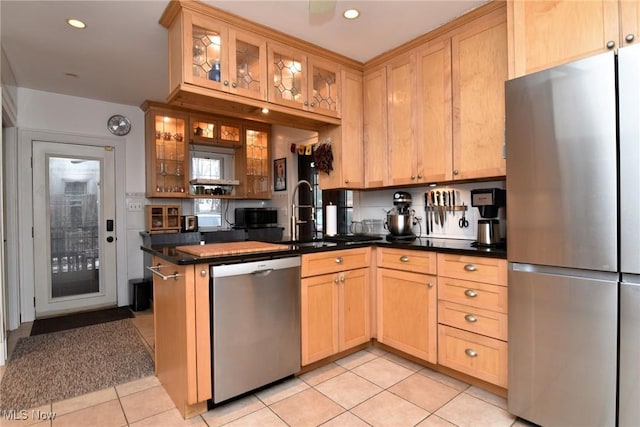 kitchen featuring dark countertops, light tile patterned floors, appliances with stainless steel finishes, and glass insert cabinets