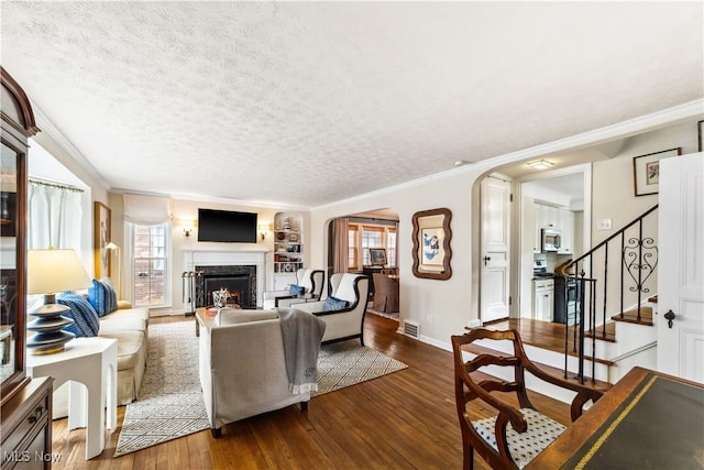 living area with dark wood-style floors, arched walkways, a warm lit fireplace, and a healthy amount of sunlight