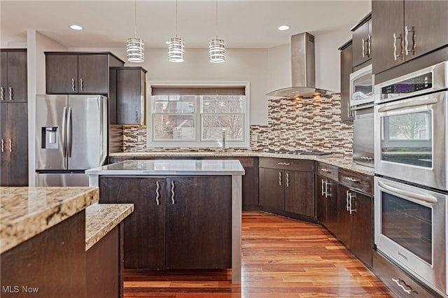 kitchen featuring dark brown cabinetry, light wood finished floors, wall chimney exhaust hood, and stainless steel appliances