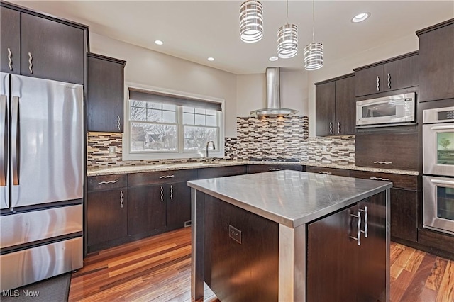 kitchen with stainless steel appliances, wall chimney range hood, a kitchen island, and light wood-style floors