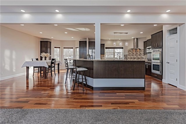 kitchen with tasteful backsplash, a healthy amount of sunlight, dark brown cabinets, and wall chimney exhaust hood