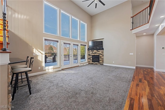 unfurnished living room with a ceiling fan, a stone fireplace, and baseboards