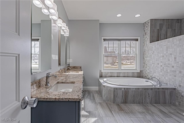 full bath featuring a bath, double vanity, a sink, and recessed lighting