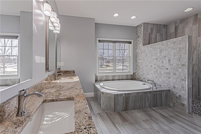 bathroom with double vanity, a tub with jets, walk in shower, and a sink