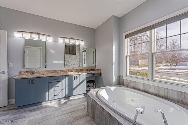 full bathroom featuring double vanity, a jetted tub, plenty of natural light, and a sink