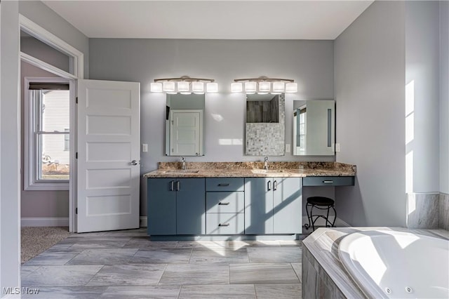 full bath with a jetted tub, double vanity, baseboards, and a sink