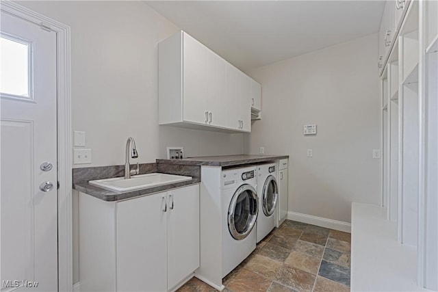 clothes washing area with washing machine and clothes dryer, cabinet space, stone finish floor, a sink, and baseboards