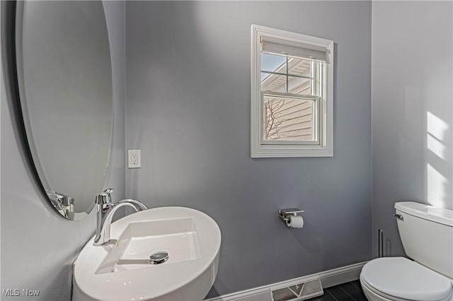 half bathroom with toilet, visible vents, baseboards, and a sink