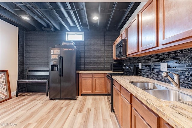 kitchen with brown cabinets, decorative backsplash, light wood-style floors, a sink, and black appliances