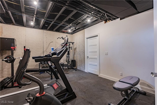 exercise area featuring baseboards and brick wall