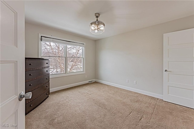 unfurnished bedroom featuring light carpet, baseboards, and an inviting chandelier