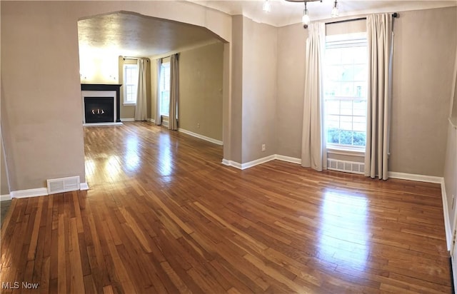 unfurnished living room featuring arched walkways, a fireplace, wood-type flooring, visible vents, and baseboards