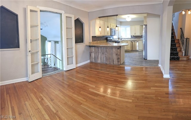 kitchen with hardwood / wood-style flooring, stainless steel appliances, a peninsula, white cabinets, and baseboards