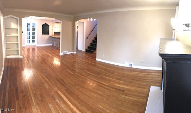 unfurnished living room with arched walkways, visible vents, baseboards, stairs, and dark wood-style floors