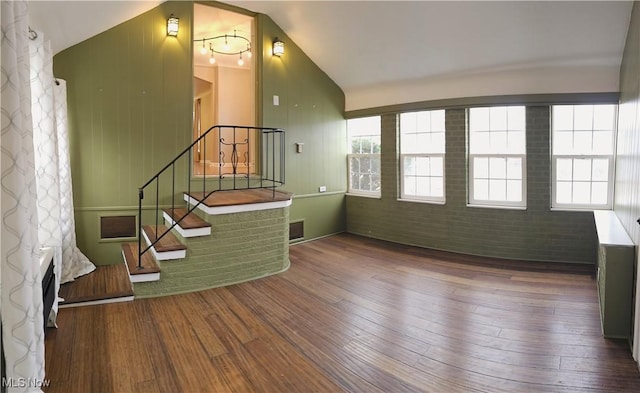 living room featuring visible vents, stairway, vaulted ceiling, brick wall, and wood finished floors