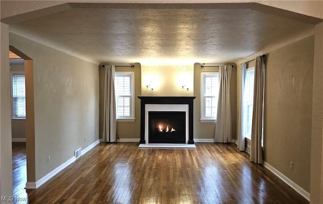 unfurnished living room with a warm lit fireplace, a wealth of natural light, wood-type flooring, and visible vents